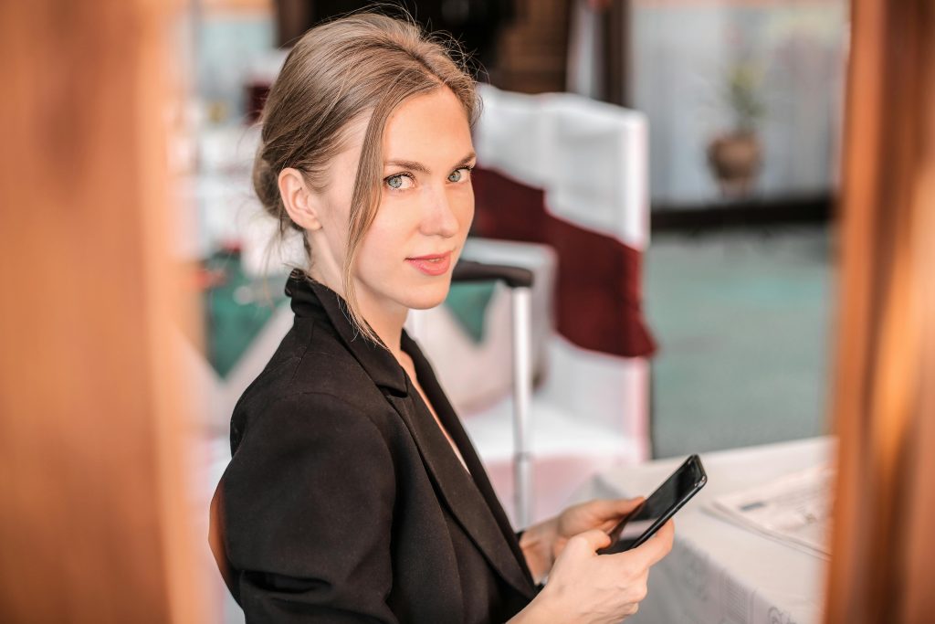 Young businesswoman using smartphone indoors with confident expression. Modern and professional setting.